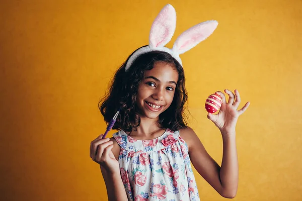 A happy girl painting Easter eggs over color background — Stock Photo, Image