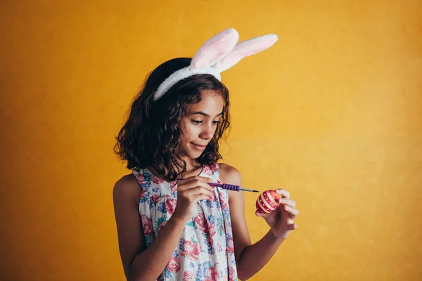 Una chica feliz pintando huevos de Pascua sobre fondo de color — Foto de Stock