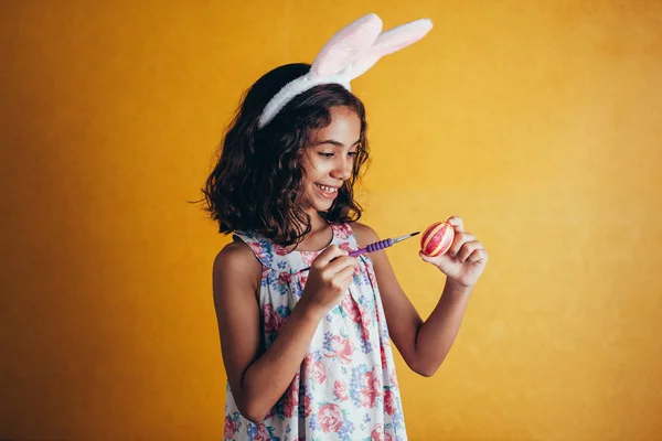 Una chica feliz pintando huevos de Pascua sobre fondo de color — Foto de Stock