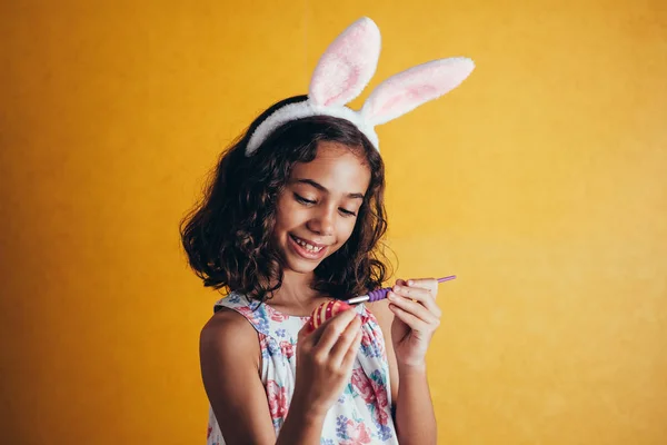 A happy girl painting Easter eggs over color background — Stock Photo, Image