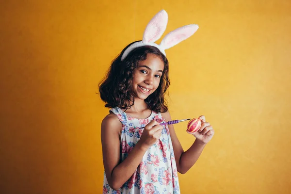 Счастливая девушка рисует пасхальные яйца на цветном фоне — стоковое фото