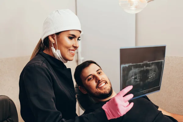 Zubař hovoří s pacientem a zobrazuje rentgram v — Stock fotografie