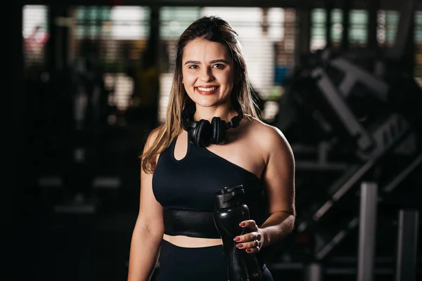 Μια νεαρή γυναίκα που κάνει ένα διάλειμμα στο γυμναστήριο με ένα μπουκάλι νερό ή ενεργειακό ποτό — Φωτογραφία Αρχείου