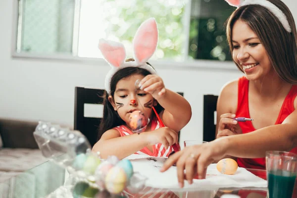 Happy easter! A mother and her daughter painting Easter eggs. Happy family preparing for Easter. Cute little child girl wearing bunny ears on Easter day — Stock Photo, Image