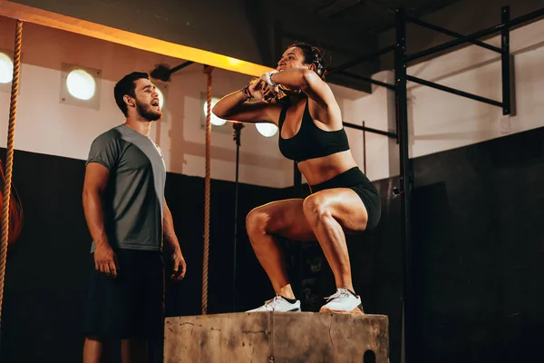 Ajuste mujer joven haciendo un ejercicio de salto de caja. Deportiva haciendo una sentadilla en el gimnasio —  Fotos de Stock