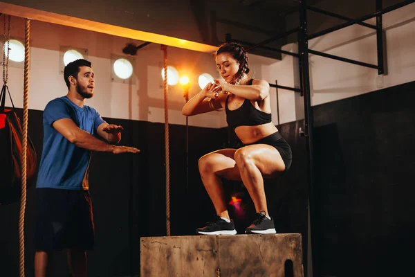 Ajuste mujer joven haciendo un ejercicio de salto de caja. Deportiva haciendo una sentadilla en el gimnasio —  Fotos de Stock