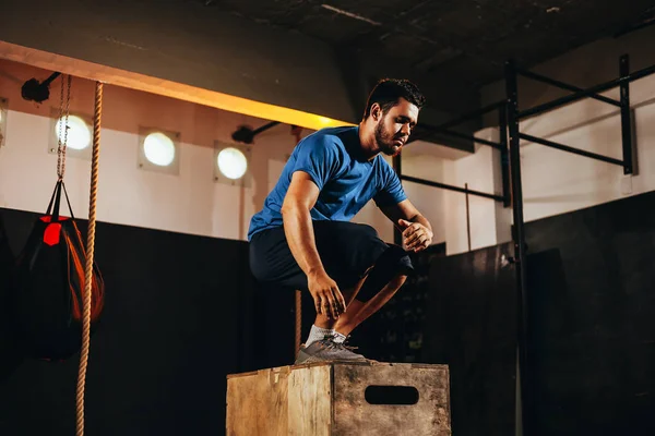 Encaixe jovem fazendo um exercício de salto de caixa. Homem de esportes fazendo um agachamento de caixa no ginásio — Fotografia de Stock