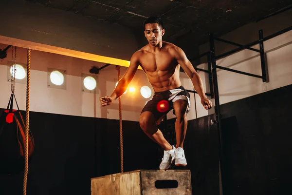 Fit young man doing a box jump exercise. Sports man doing a box squat at the gym