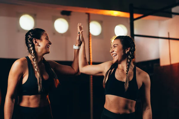 Mujeres sonrientes haciendo choca esos cinco en el gimnasio. Joven mujer haciendo alta cinco gesto en el gimnasio después del entrenamiento —  Fotos de Stock