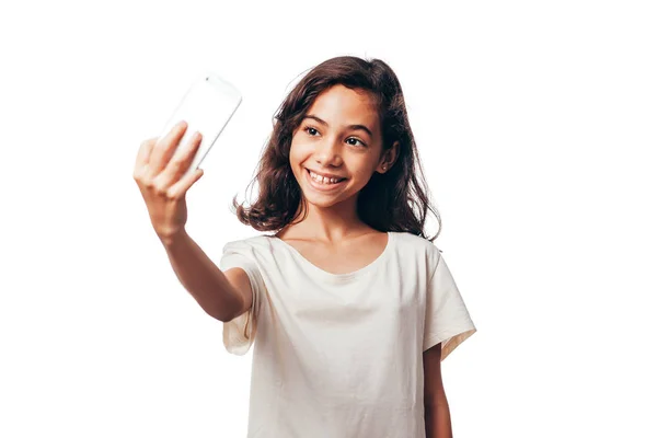 Retrato de una niña sonriente sosteniendo el teléfono móvil y haciendo selfie aislado sobre fondo blanco —  Fotos de Stock