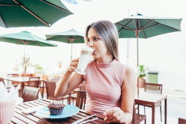 Genç bir kadın kahve ve pastayla kahvaltı yapıyor.