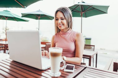 Bir kafede dizüstü bilgisayar kullanan güzel genç kadın