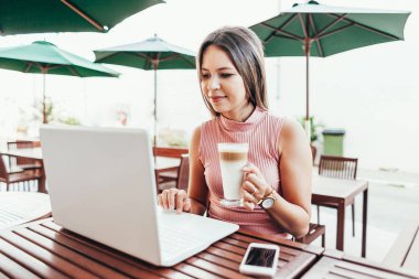 Bir kafede dizüstü bilgisayar kullanan güzel genç kadın