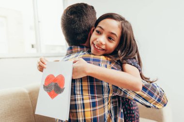 Babalar günün kutlu olsun! Kızı babamı tebrik ediyor ve ona tebrik kartı veriyor. Baba ve kızı gülümsüyor ve sarılıyor. Aile tatili ve birliktelik