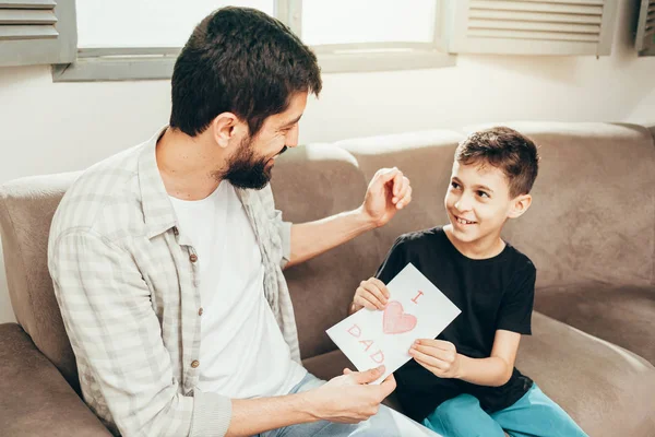 Happy father\'s day! Son congratulating dad and giving him a greeting card. Daddy and son smiling and hugging. Family holiday and togetherness.