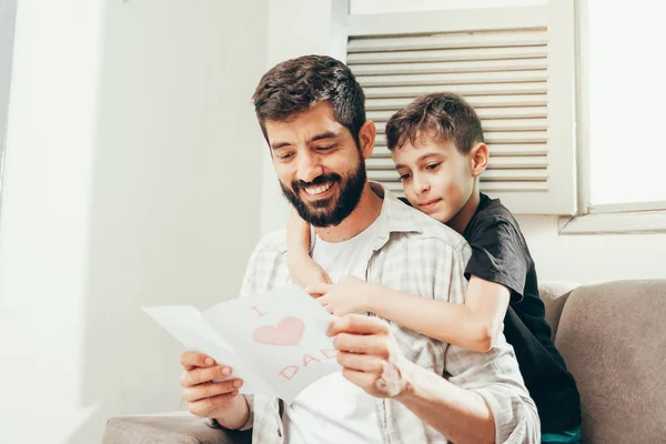 Happy vader Day! Zoon feliciteren vader en het geven van hem een wenskaart. Papa en zoon glimlachen en knuffelen. Familie vakantie en saamhorigheid. — Stockfoto