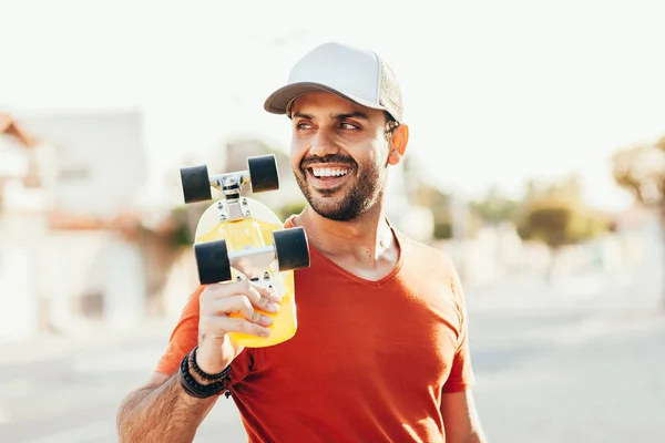 Portrét mladého pohledného muže, který drží skateboard ve městě — Stock fotografie