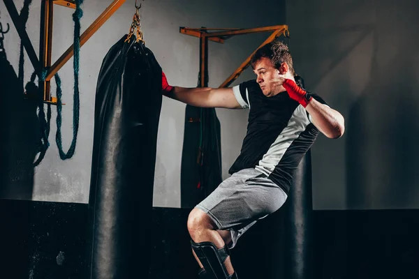 Lutador kickbox muscular exercitando com saco de soco no ginásio — Fotografia de Stock