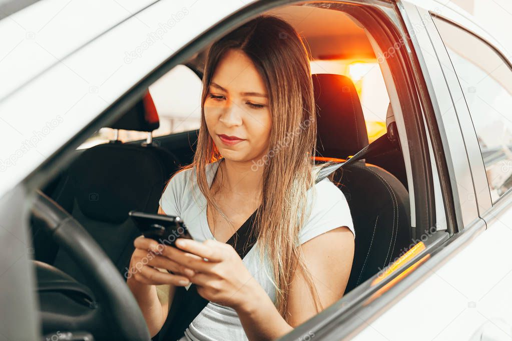 Woman driver sitting behind the steering wheel reading a text me
