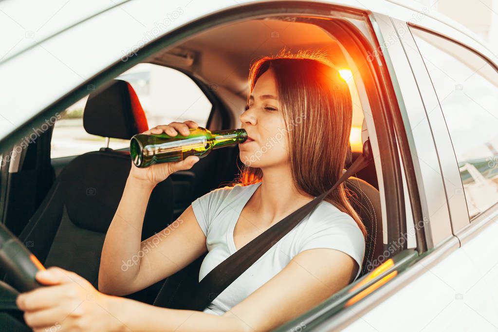 Drunk young woman drives a car with a bottle of beer