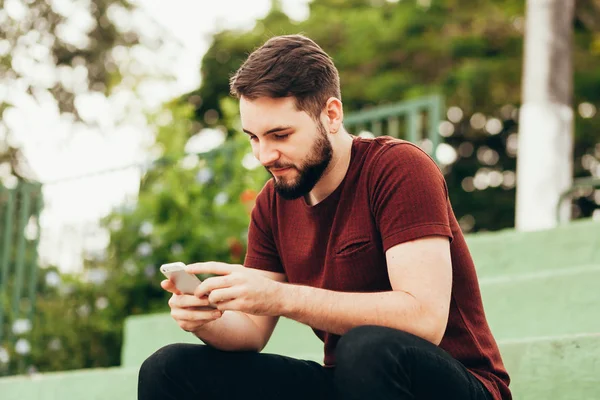 Привабливий молодий усміхнений чоловік використовує телефон у громадському парку — стокове фото