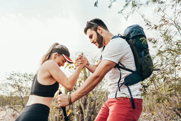 Ein männlicher Wanderer hilft seiner Freundin auf dem Land bergauf. Sie — Stockfoto