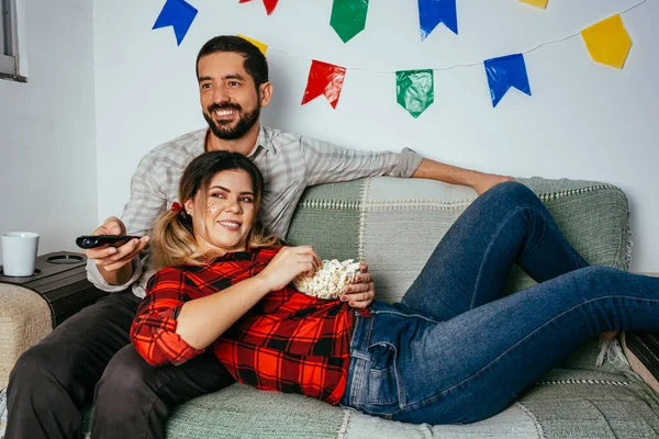ブラジル フェスタ ジュニーナの自宅 典型的な服を着ている人 カラフルな旗で飾られたリビングルーム 夫婦テレビを見て — ストック写真