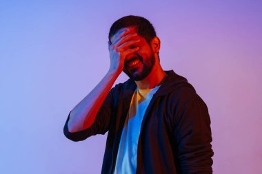 Utanmış bir adamın neon ışıklı portresi yüzünü örtüyor ve gülüyor.