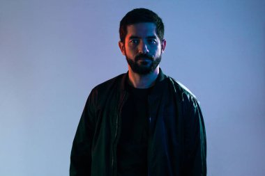 Mavi ve kırmızı ışıklarla aydınlatılmış ceketli bir adamın dramatik portresi.