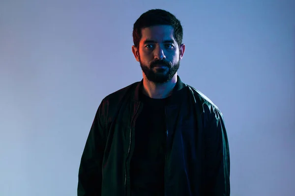 Dramatic portrait of man wearing jacket lit by blue and red lights.