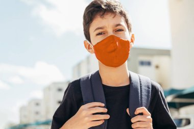 Dışarıda sırt çantalı, yüz koruma maskesi takan 10 yaşında bir çocuk. COVID-19 salgını sırasında okula dönüş kavramı.
