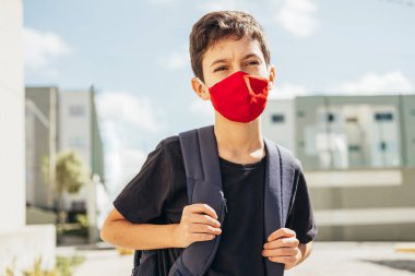 Dışarıda sırt çantalı, yüz koruma maskesi takan 10 yaşında bir çocuk. COVID-19 salgını sırasında okula dönüş kavramı.
