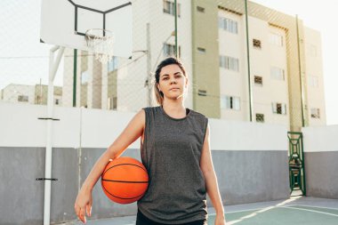 Spor giyimli genç Latin kadın dışarıda basketbol oynuyor.