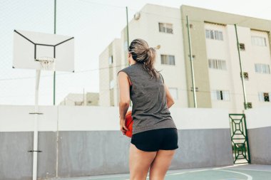 Spor giyimli genç Latin kadın dışarıda basketbol oynuyor.