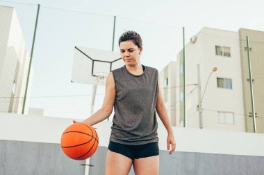 Spor giyimli genç Latin kadın dışarıda basketbol oynuyor.
