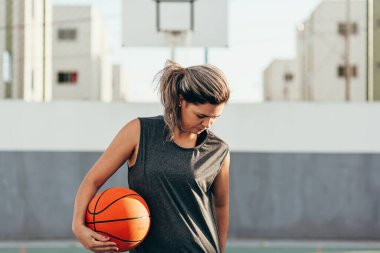 Spor giyimli genç Latin kadın dışarıda basketbol oynuyor.