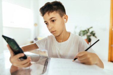 Çocuklar, eğitim ve teknoloji konsepti - akıllı telefon öğrenimi evde olan öğrenci