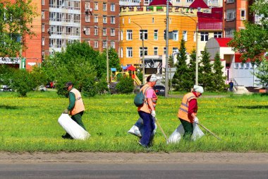 Krasnoyarsk, Rusya, 7 Haziran 2018: Yelek yolun yanındaki çim üzerinde çöp toplamak süpürgeler turuncu sinyal. Gerçek hayat. Sahne sahnelenen değil