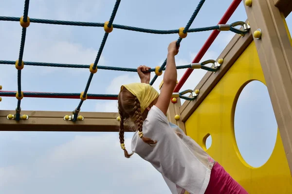 シャツ 赤いおさげの黄色いハンカチを持つ少女は 子供の遊び場に彼女の手を保持ロープ メッシュの運動を実行します 背面からクローズ アップ ビュー — ストック写真