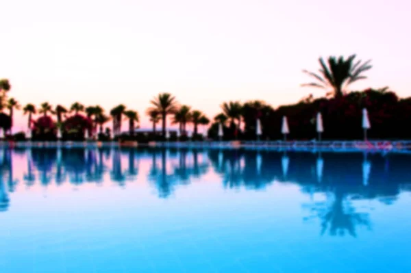 Beautiful blurred background of the pool water on vacation. Palm trees with reflection in water. Beautiful background on the theme of recreation travel and tourism.