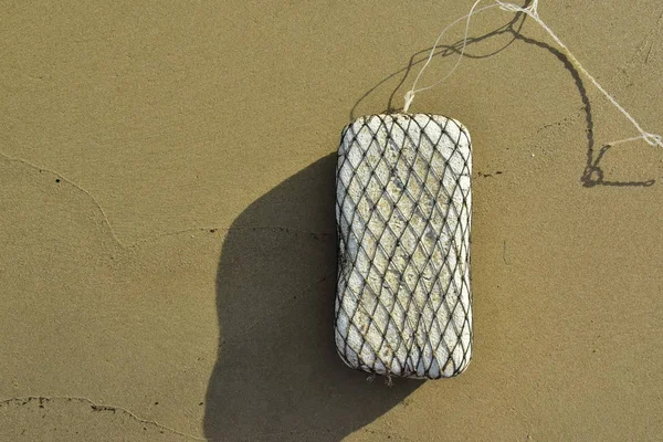 Self-made white polystyrene buoy a tied to a rope network fishing fish on a wet sand background ocean design beach fishing village. Garbage thrown ashore by waves