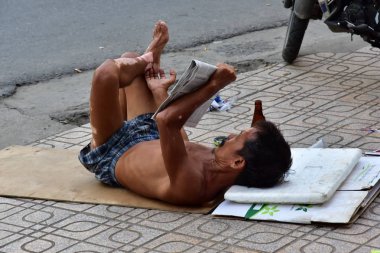 12 Temmuz 2018. Nha Trang. Vietnam. Bir sokak dilenci yerde yatıyor. En son haberleri gazete okuyor. Onun deri hastalık ile ele alınacaktır.