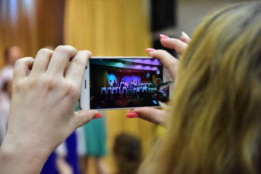 Bir kadın bir smartphone cep telefonu ile bir konserde çocuğunun performans vuruyor. Tırnaklarına pembe boyanır. Video kızı için hatırlanacak