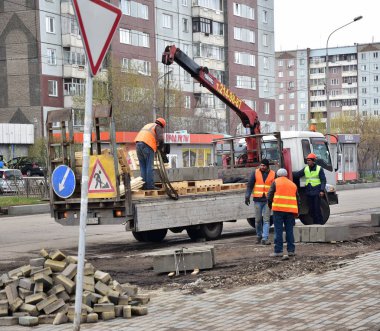Krasnoyarsk, Rusya, 9 Mayıs 2018: Turuncu renkli yelek inşaat kuruluşta işçilerin paletleri ile yolun onarmaya curbs kaldırmak için bir vinç kullanın
