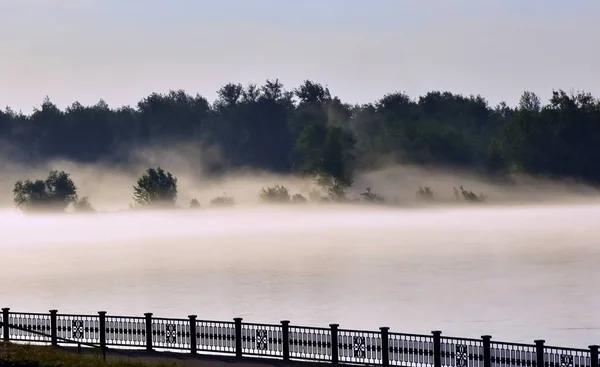 The Yenisei River and the forest in the fog. Against the background of the river silhouette of steel fence. Krasnoyarsk. Russia