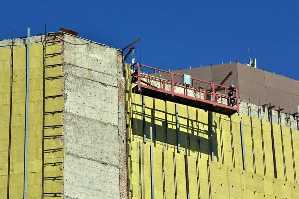 High-altitude work on the external walls of glass wool insulation. Workers use special equipment to insulate the facade of the building and finish it with panels