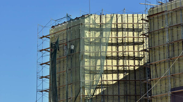 High-altitude work on the external walls of glass wool insulation. Workers using the scaffolding and special equipment perform the insulation of the facade of the building