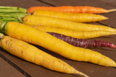 Bir sürü ahşap arka plan üzerinde temiz taze havuç. bir portakal ve sarı arasında bir mor havuç