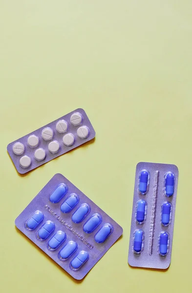 Three packing of blue tablets with copy space on yellow background. Medical concept treatment of diseases, sale of tablets, tablets in blister pack. Top view