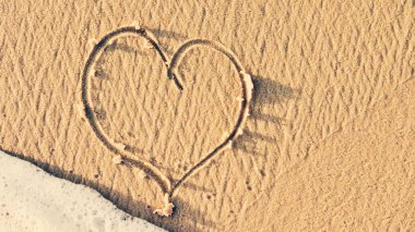 Sahilde bir kalp ve arka planda dalgalar.